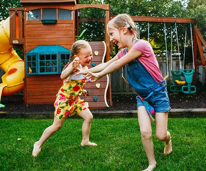 Fröhlich spielende Kinder vor einer Spielgeräte-Kombination im Garten